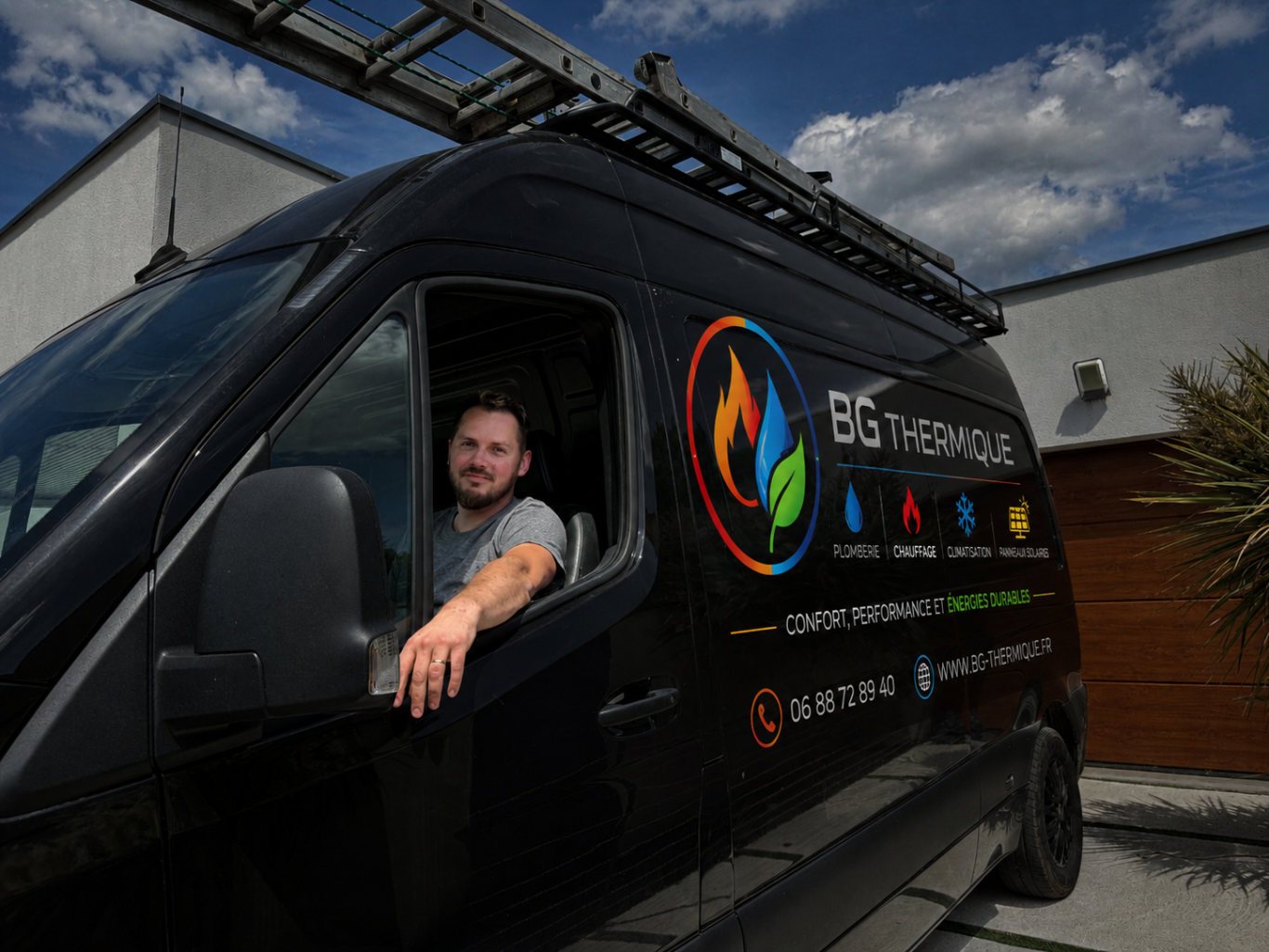 Homme dans un camion noir avec une échelle sur le toit, devant un bâtiment moderne.